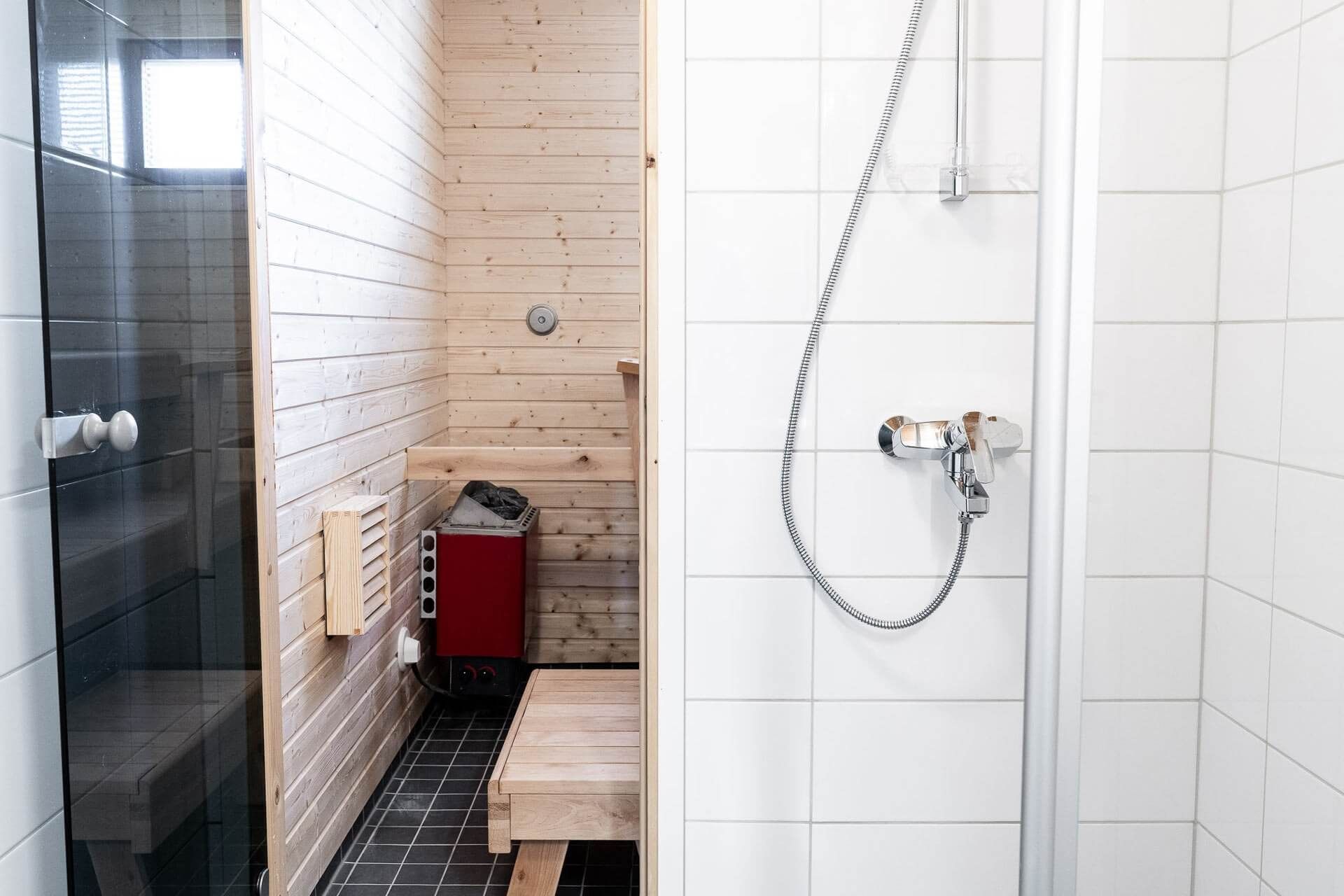 Bathroom with a sauna and shower. The sauna is wood-paneled with a red heater. The shower has white tile.