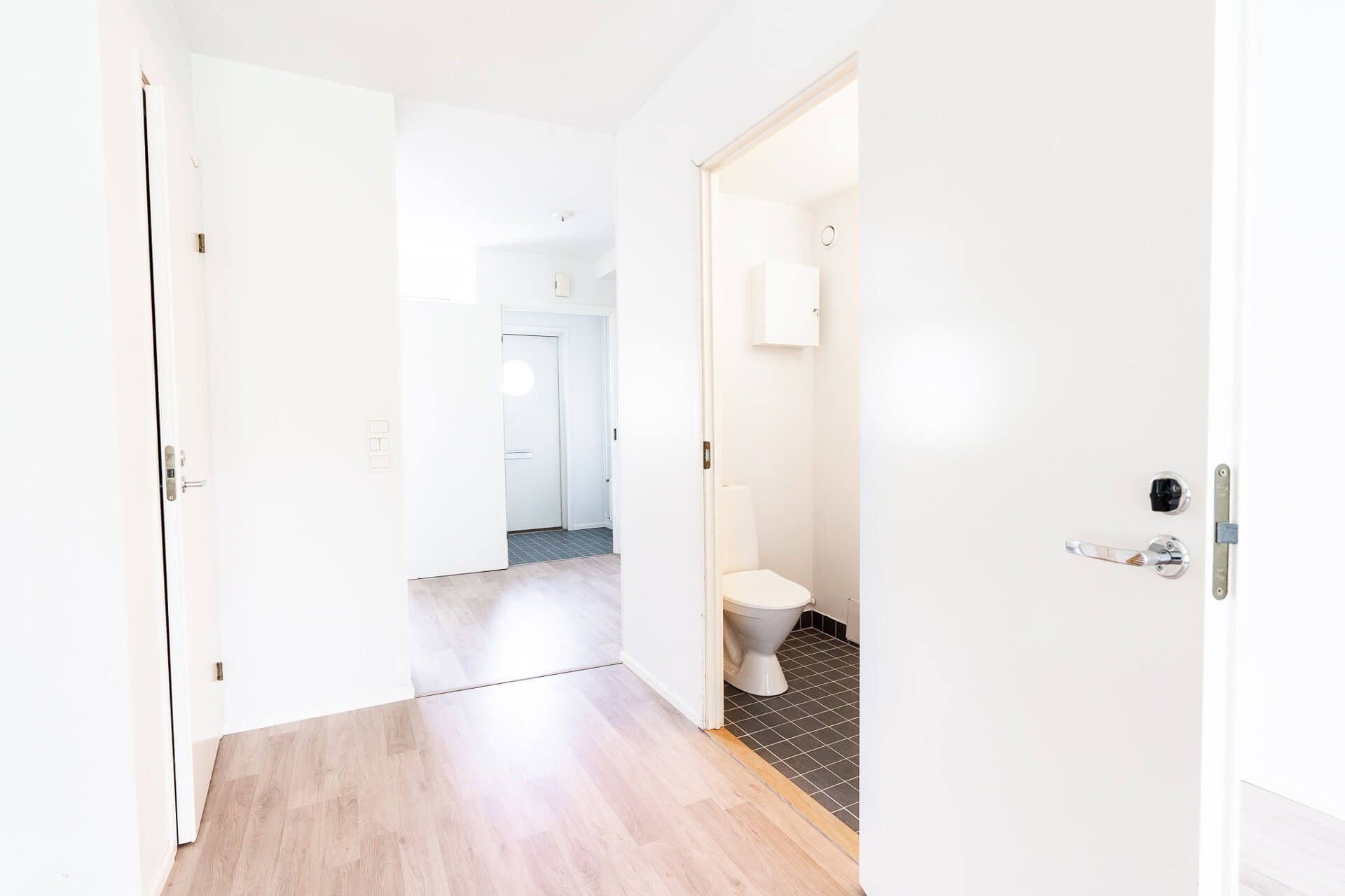 Sisäkäytävä, jossa valkoiset ovet, vaalea puulattia ja näkyvissä oleva kylpyhuone.