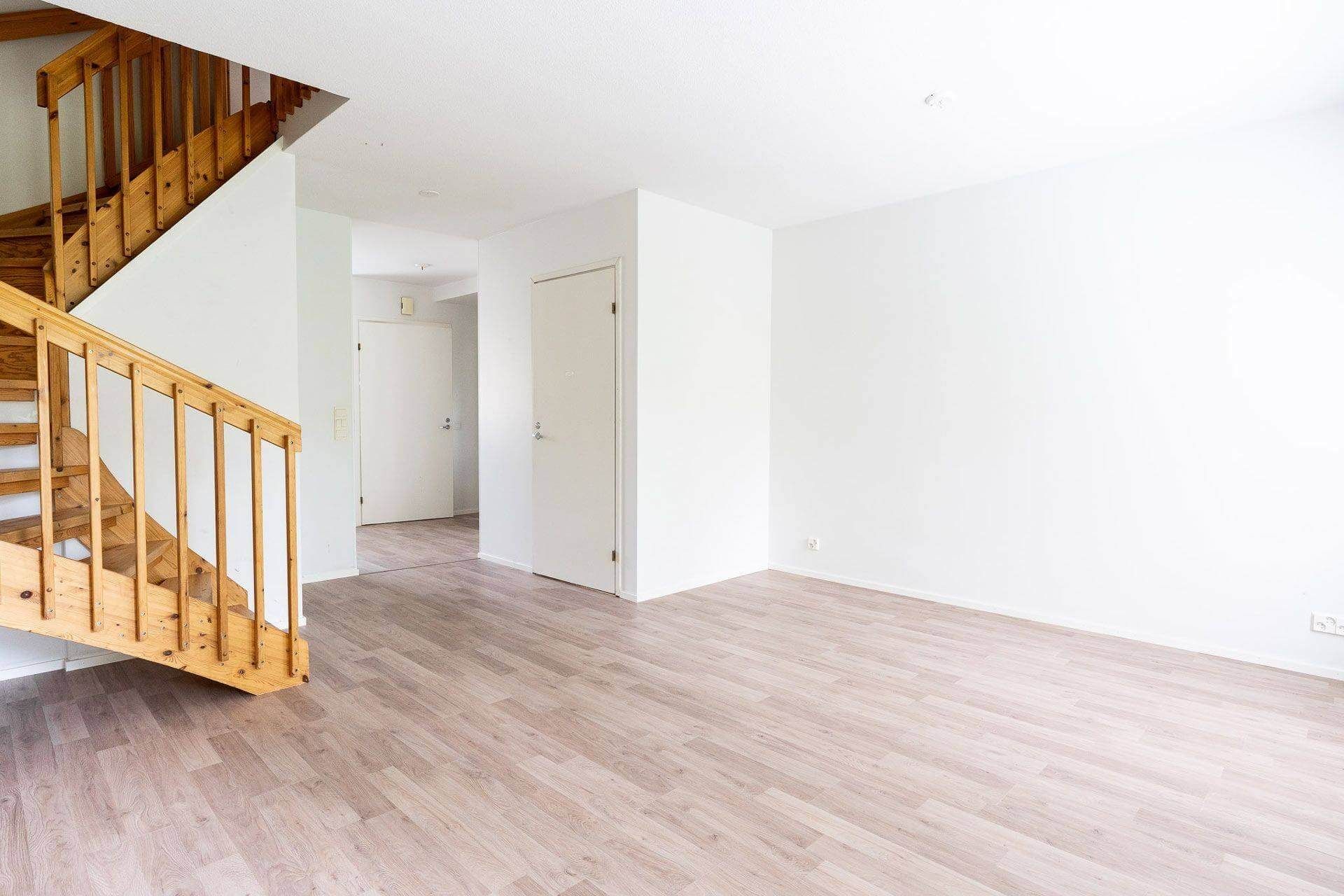 Kodin sisustus, jossa on puiset portaat, vaalea puulattia ja valkoiset seinät.