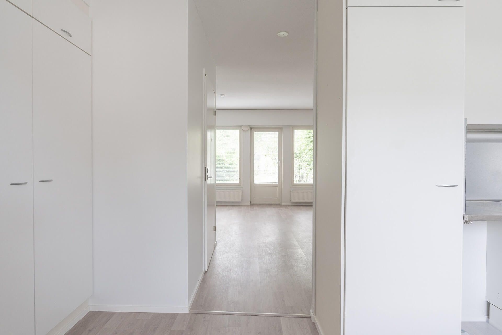 Kirkas, tyhjä asunnon käytävä, jossa on valkoiset kaapit ja näkymä ikkunoista.