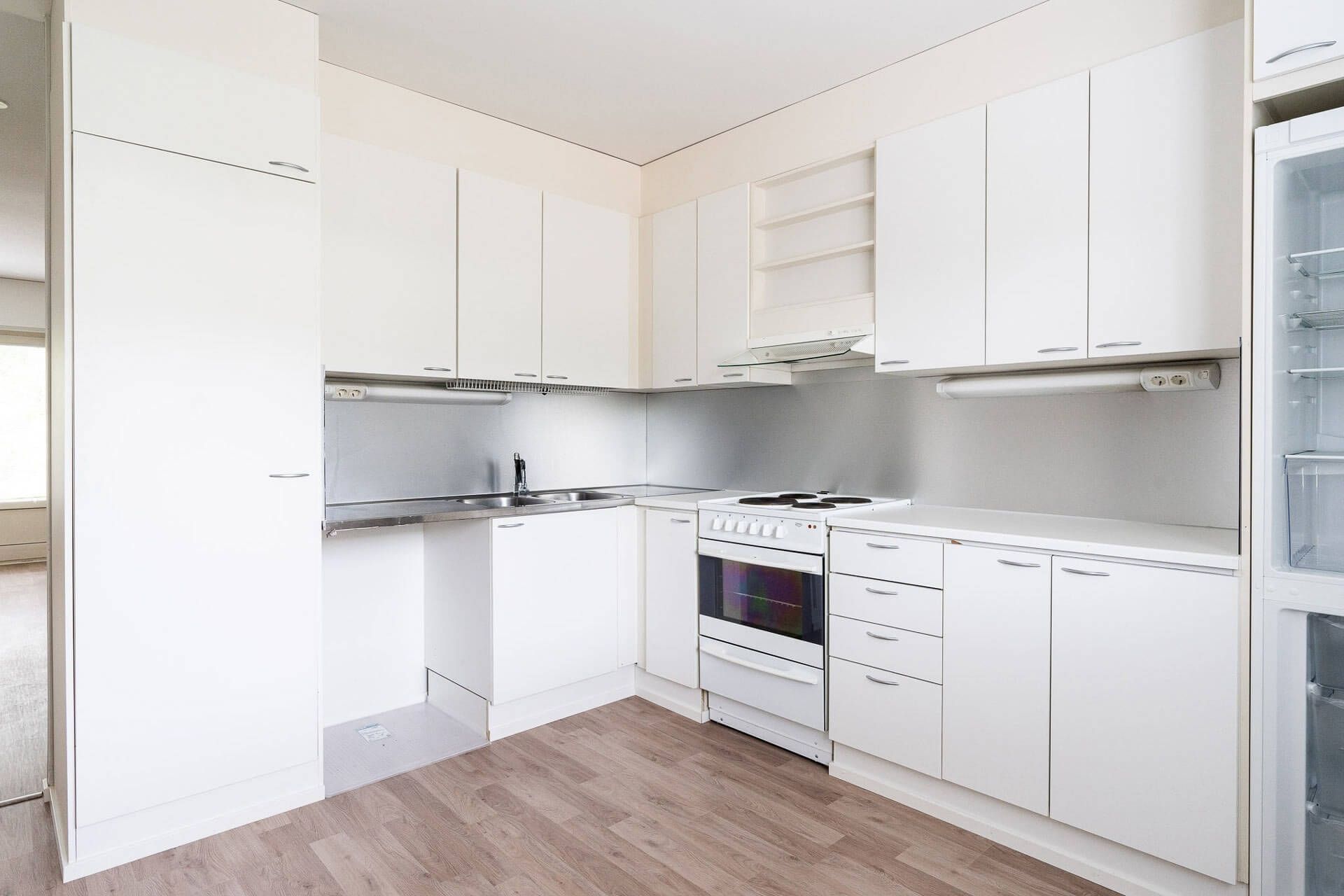 White kitchen with cabinets, stove, sink, and light-colored flooring.