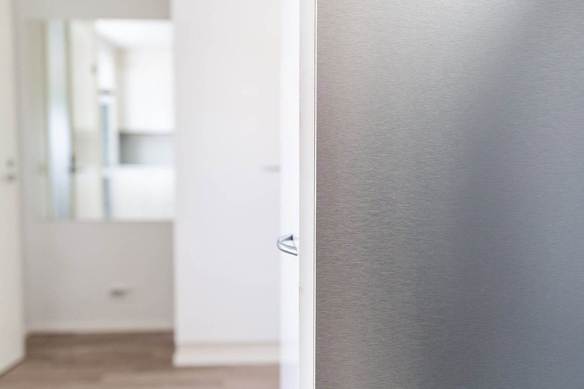 Oviaukko paljastaa valkoisen eteisen, jossa on peili, joka luo kontrastin harmaalle tekstuuripinnalle.