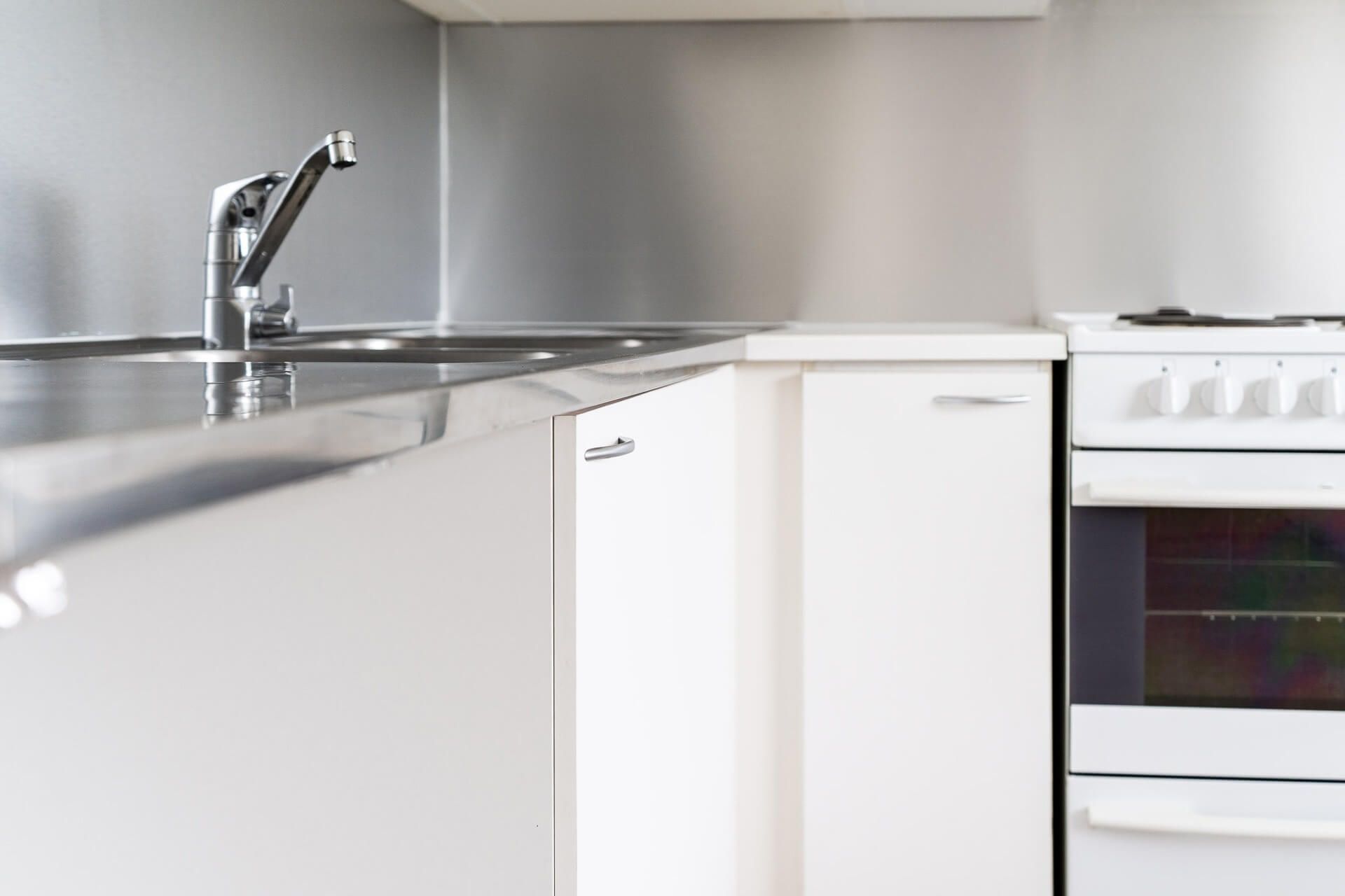 Moderni keittiö, jossa ruostumattomasta teräksestä valmistettu allas, valkoiset kaapit ja uuni hopeanväristä seinää vasten.