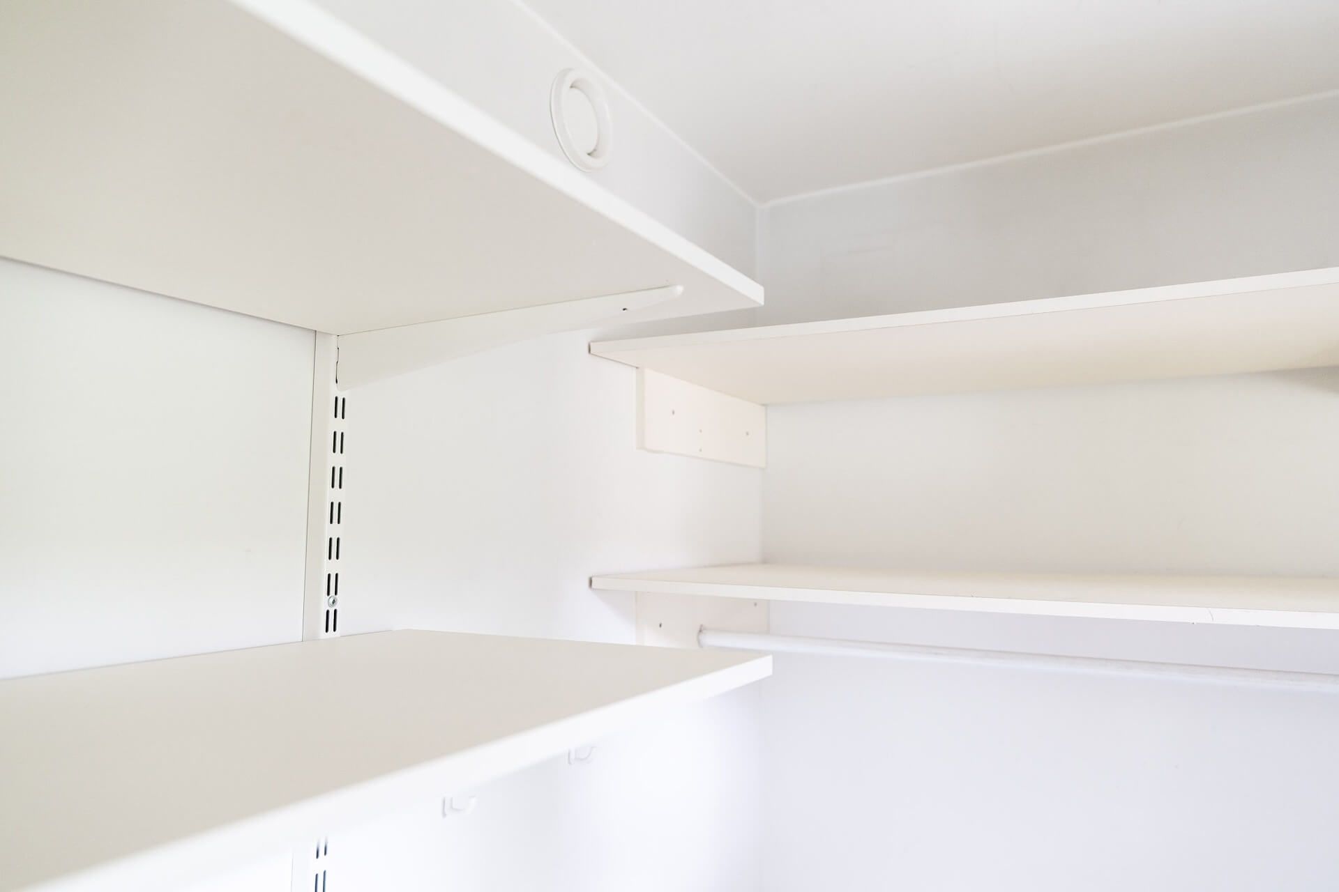Valkoiset hyllyt kaapissa. Useita hyllyjä on asennettu eri korkeuksille valkoisia seiniä vasten.