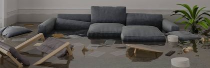 Tulviva olohuone, jossa on harmaa sohvaryhmä, veden alla olevia huonekaluja ja ruukkukasvi.