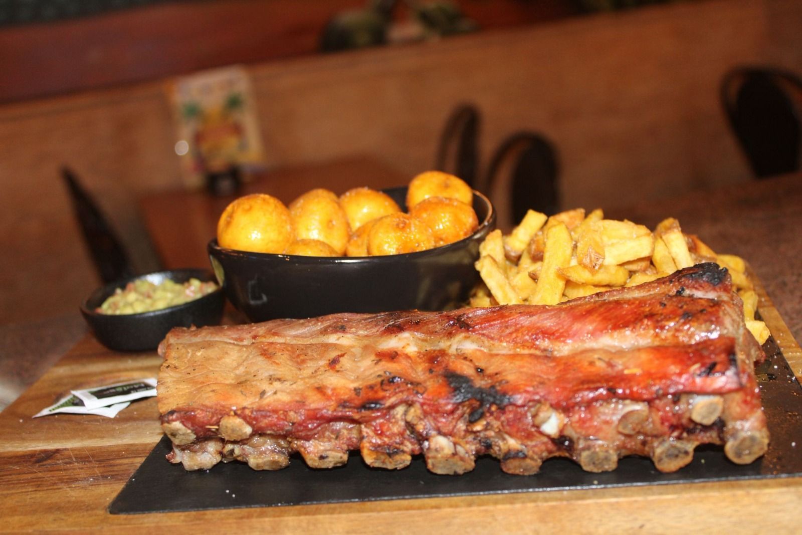 Un costillar servido en una bandeja de pizarra con un tazón de papas asadas, una guarnición de ensalada de col