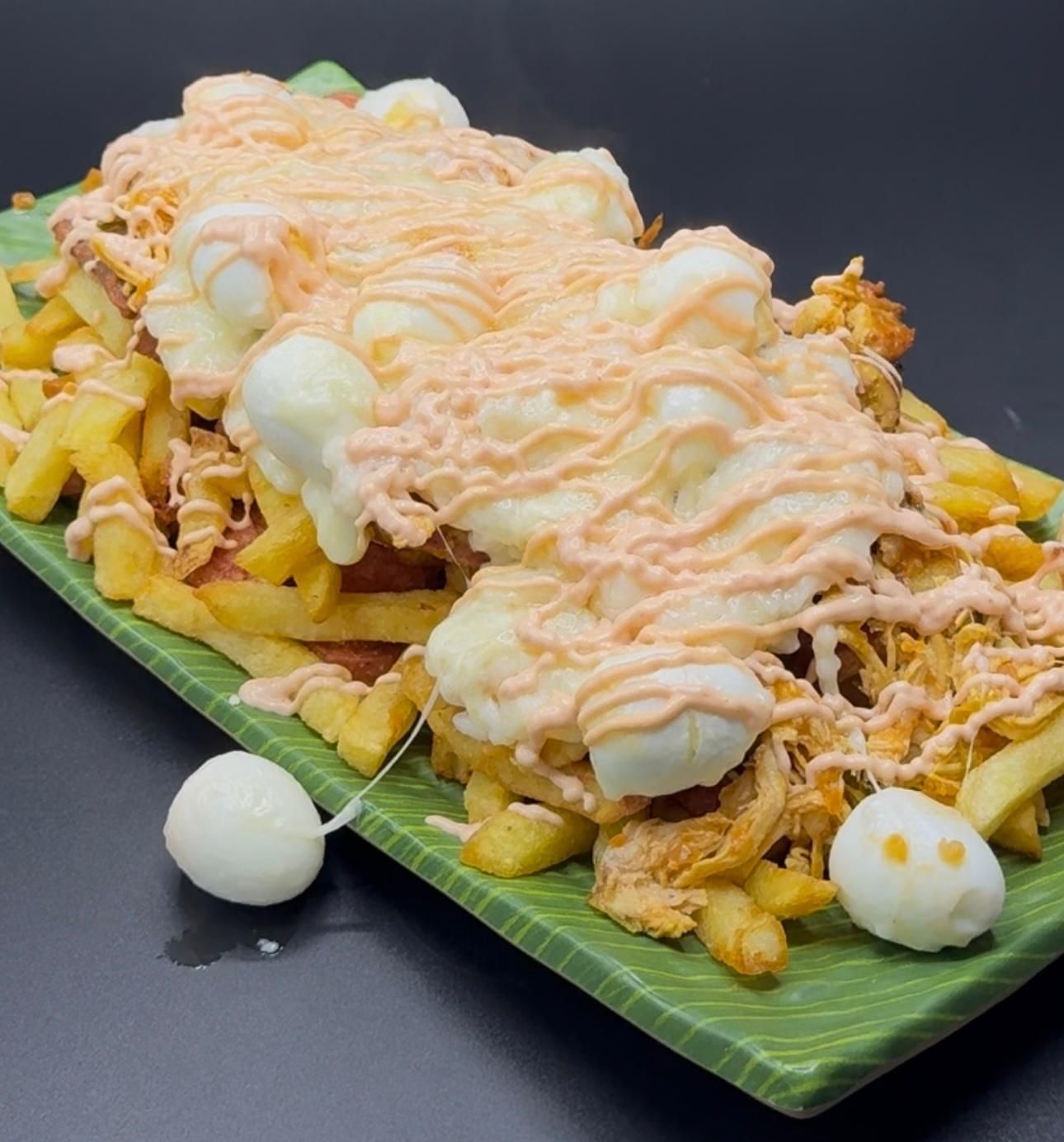 Un plato verde repleto de patatas fritas, carne desmenuzada, queso blanco fundido y huevos de codorniz