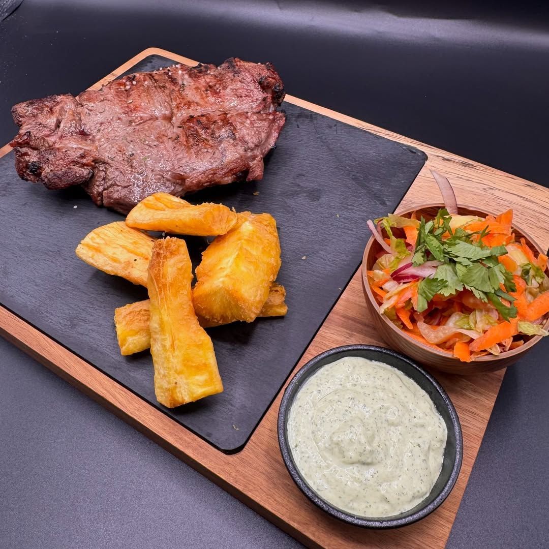 Un filete a la parrilla servido con yuca frita, una ensalada y un tazón de salsa verde