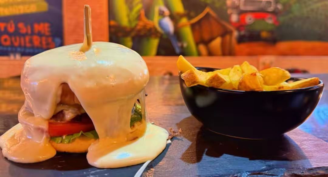 Una hamburguesa cubierta de queso fundido, ensartada con un palillo, junto a un cuenco negro de patatas fritas doradas