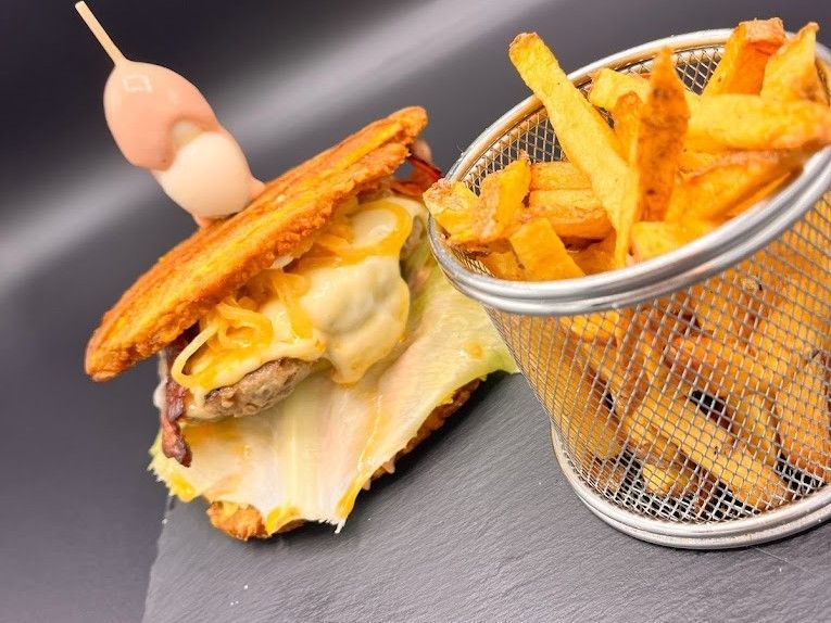 Una hamburguesa con pan de plátano frito y una cesta de alambre con patatas fritas doradas