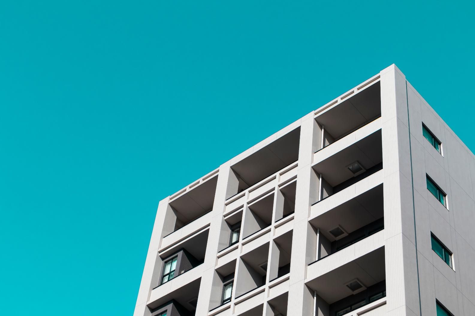 Edificio de apartamentos gris con balcones contra un cielo turquesa brillante.