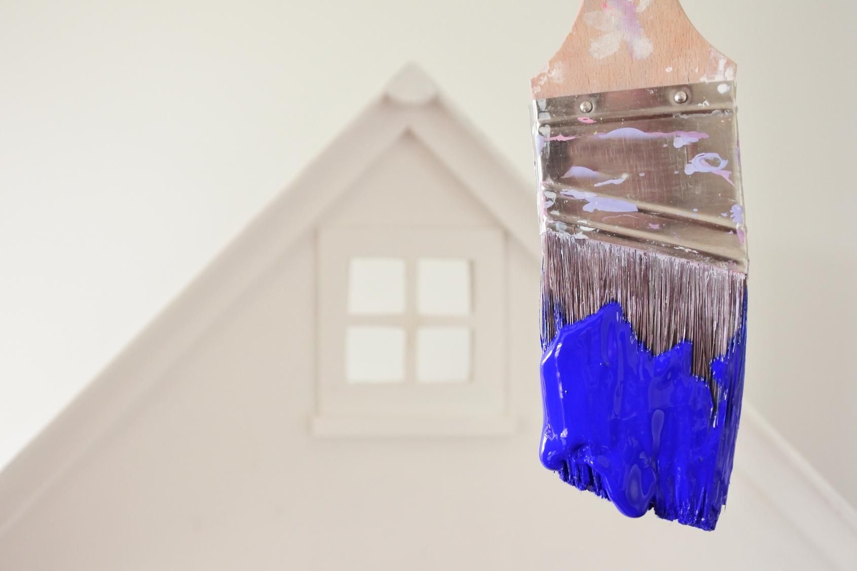 Pincel con pintura azul sobre el fondo de una casa blanca con una ventana.