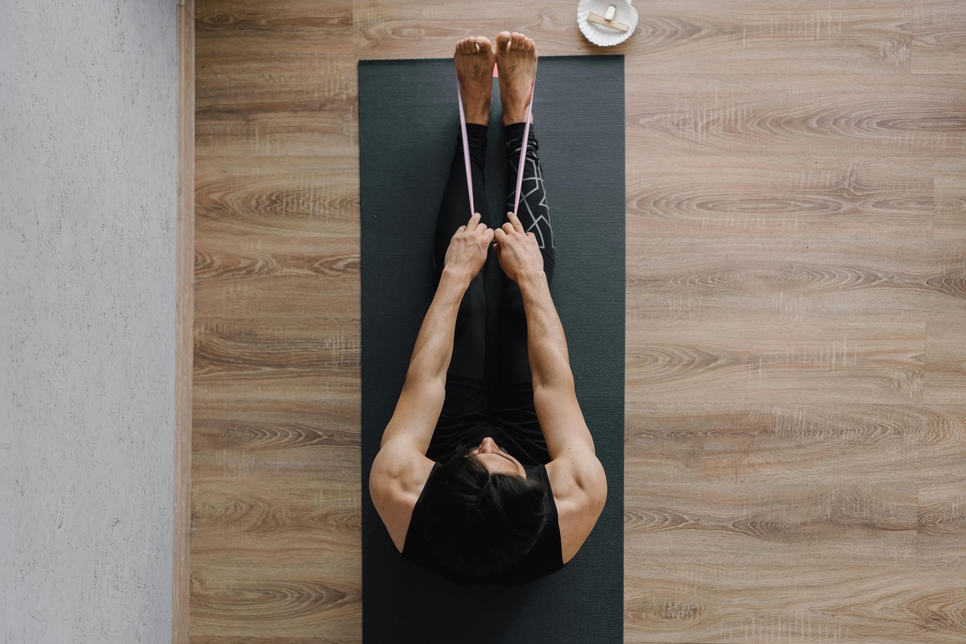 Persona sentada sobre una colchoneta de yoga, con las piernas extendidas sujetando la correa y el cuerpo formando una V.
