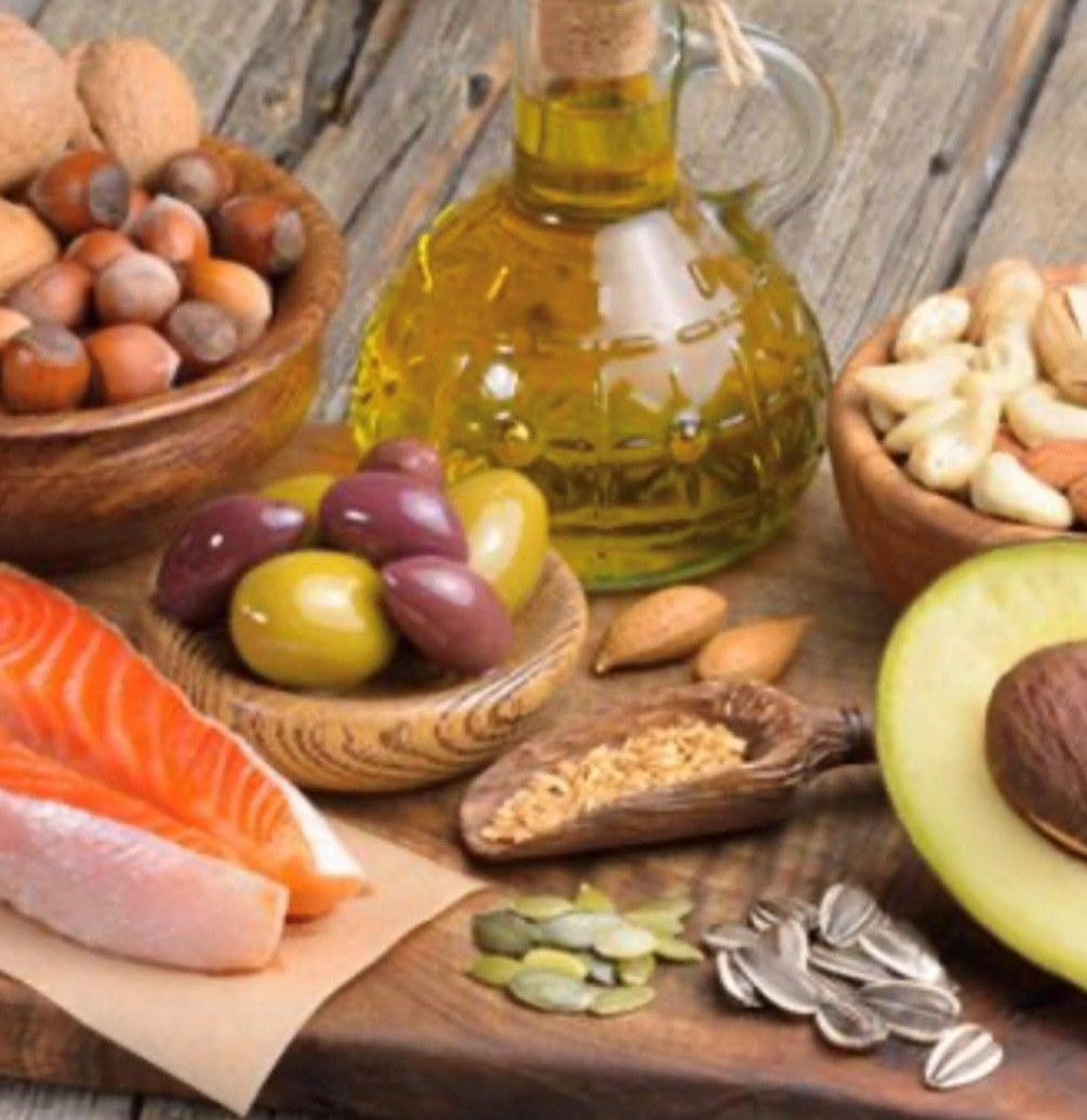 Verschiedene gesunde Fette: Lachs, Avocado, Oliven, Nüsse, Samen und Olivenöl.