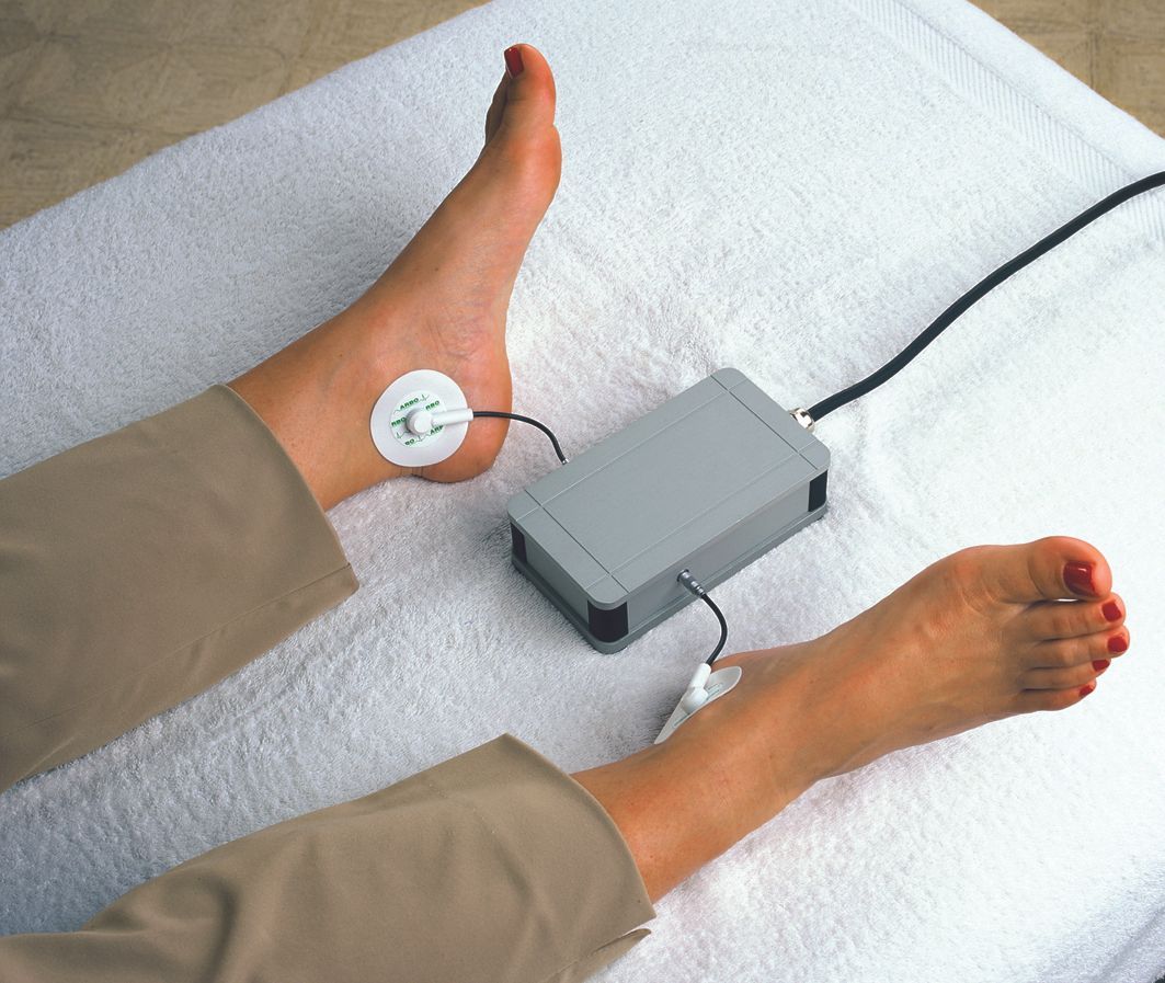 Fuß mit Knöchelelektrode, die mit einem Gerät auf einem weißen Handtuch verbunden ist.