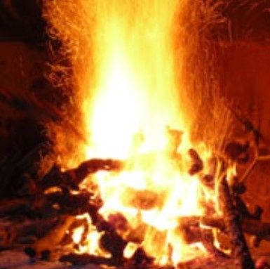 Hoguera ardiente, con llamas de color naranja y amarillo brillante que se elevan desde la madera apilada.