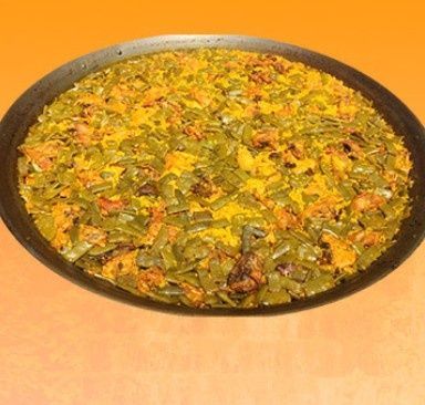 Paella en sartén grande negra; arroz amarillo, judías verdes, pollo.