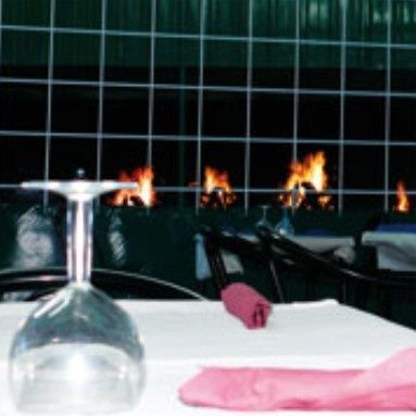 Copa de vino sobre una mesa preparada para la cena; chimenea al fondo.