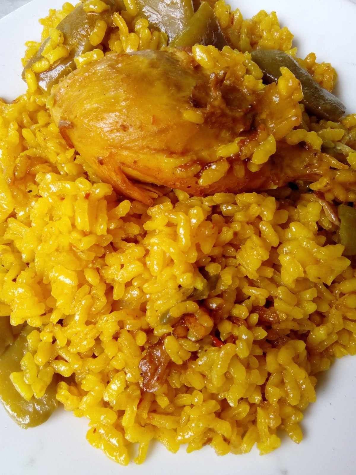 Plato de arroz amarillo con pollo y verduras verdes.