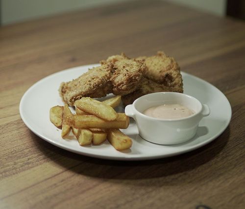 Un plato de pollo frito y papas fritas con salsa para mojar en una mesa de madera.