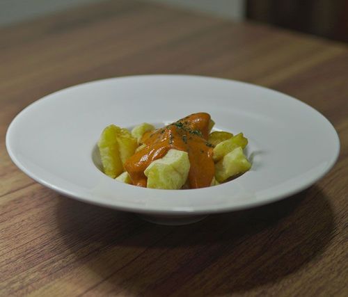 Un plato blanco cubierto con patatas y salsa sobre una mesa de madera.