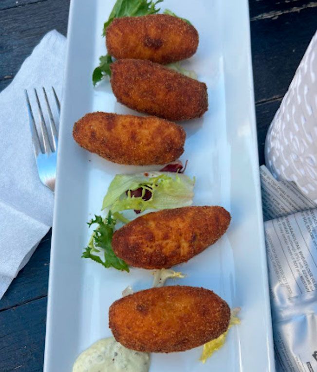 Un plato blanco cubierto con comida frita junto a un tenedor y una servilleta.