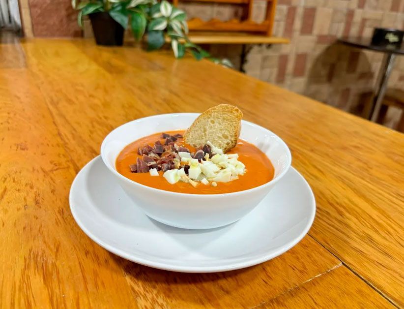 Un tazón de sopa con un trozo de pan en un plato sobre una mesa de madera.