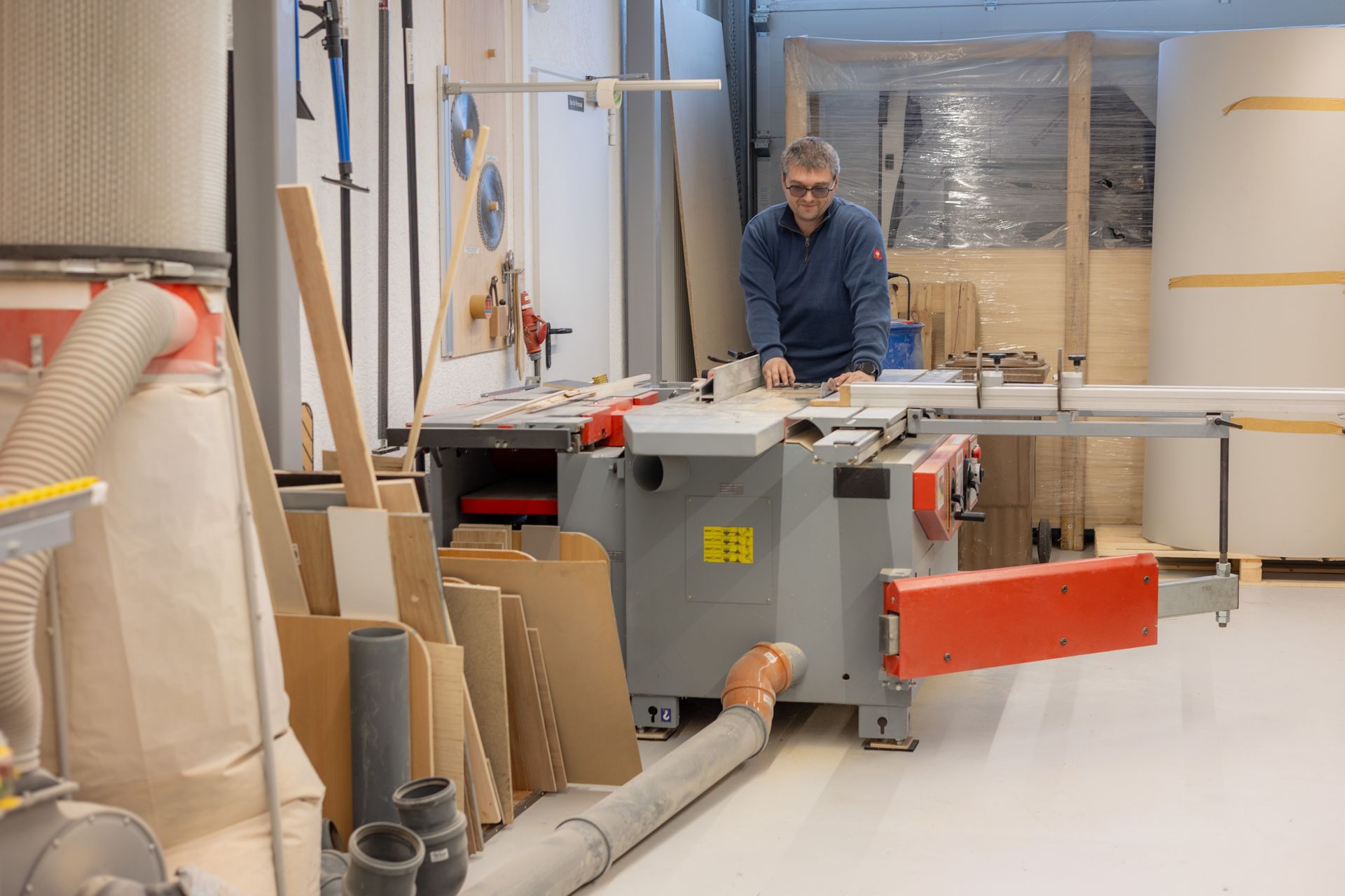 Ein Mann bedient in einer Holzwerkstatt eine Tischkreissäge und schneidet ein Stück Holz zu.