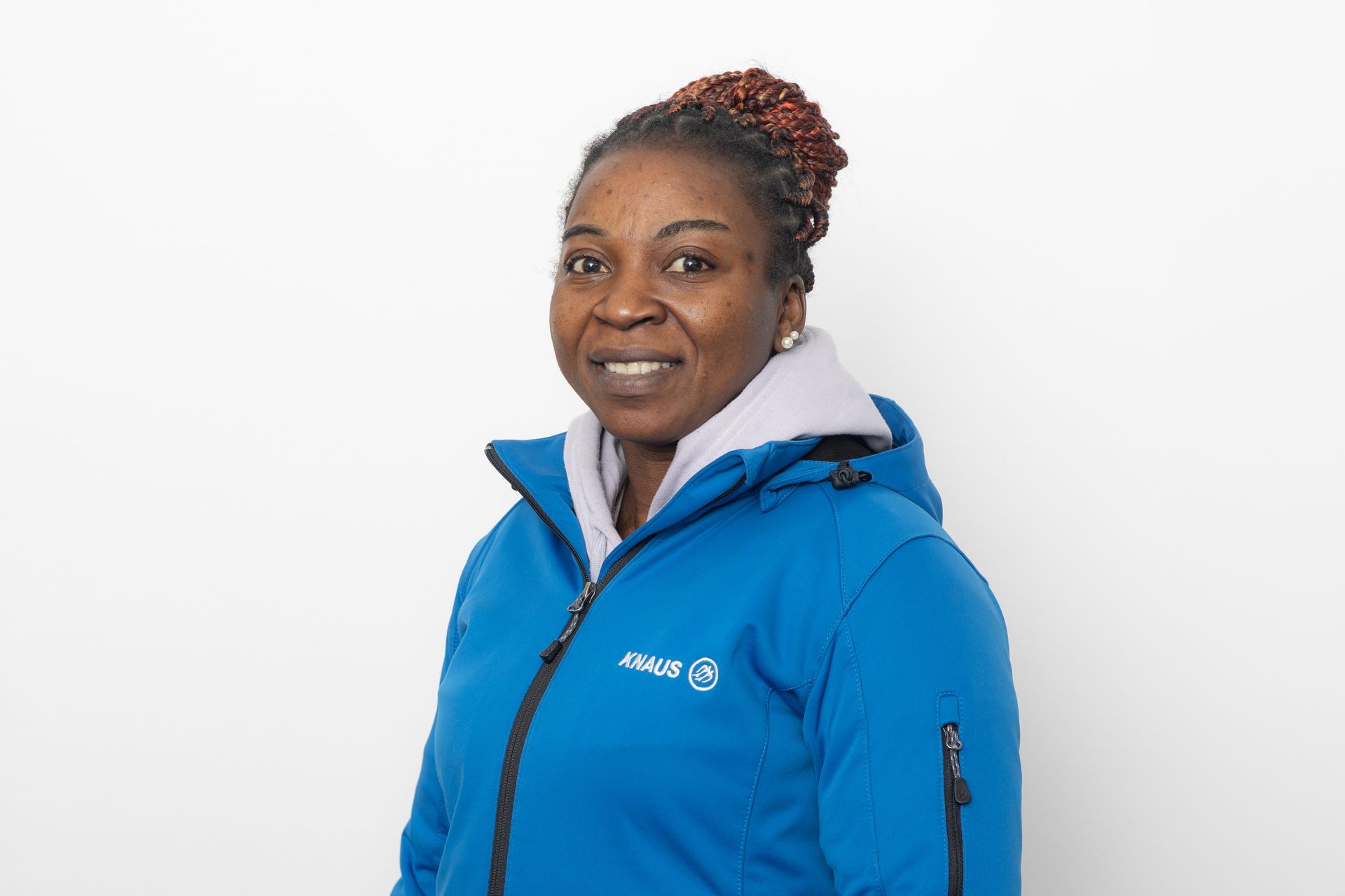 Eine Frau in blauer Jacke lächelt vor einem weißen Hintergrund.
