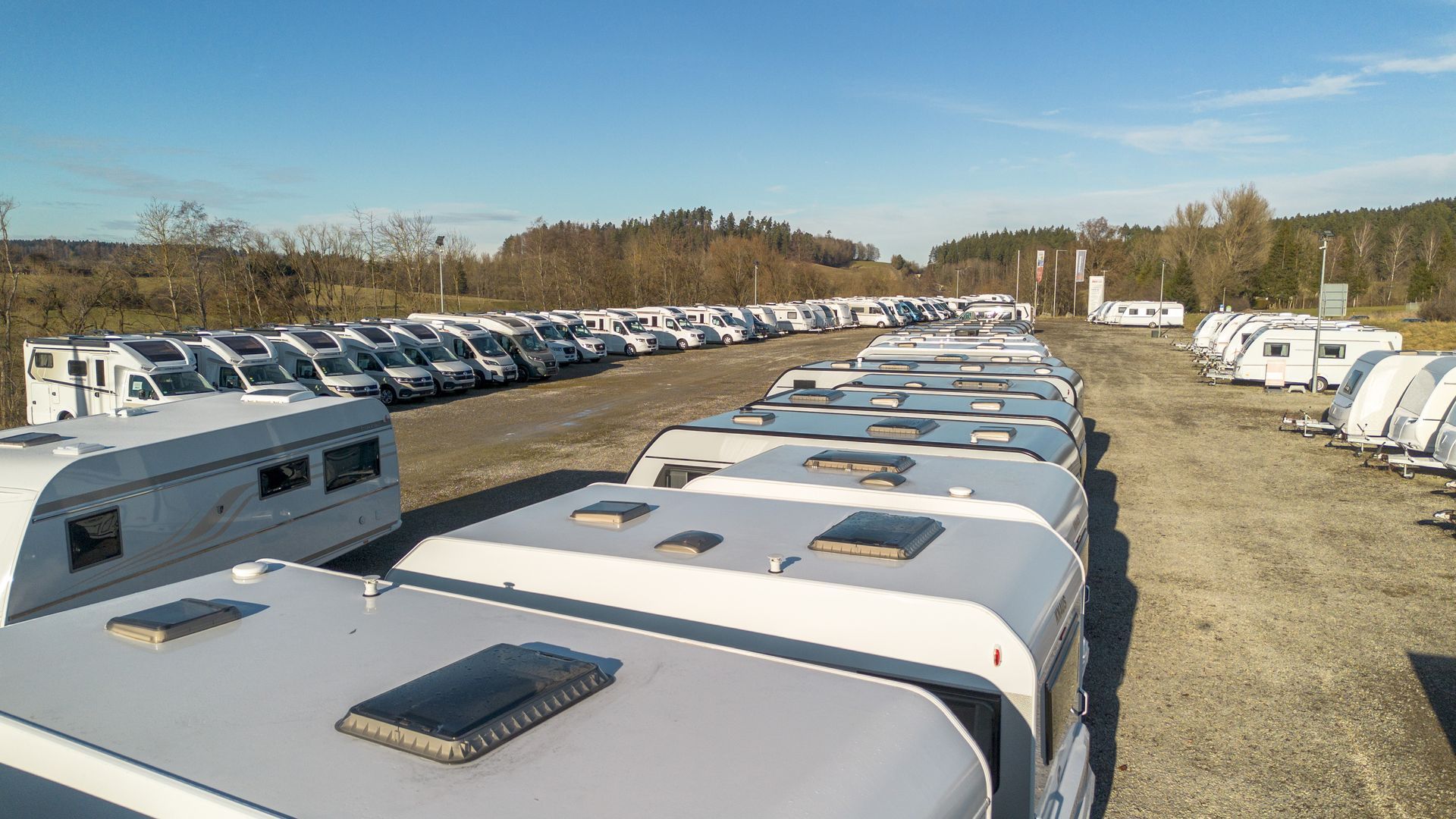 Reihen von geparkten Wohnmobilen auf einem Freiluftparkplatz an einem sonnigen Tag.