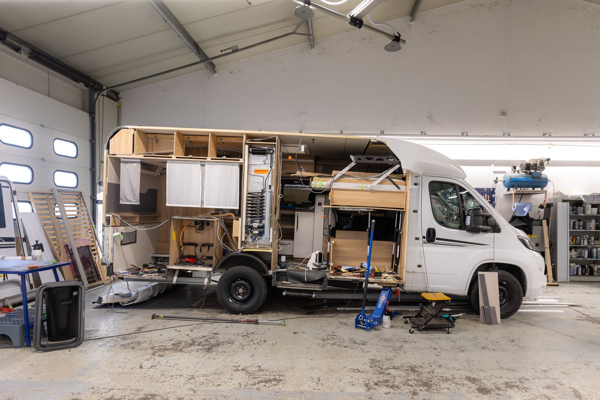 Ein weißer Campervan wird in einer Werkstatt innenausgebaut. Holzrahmen und Schränke sind sichtbar.