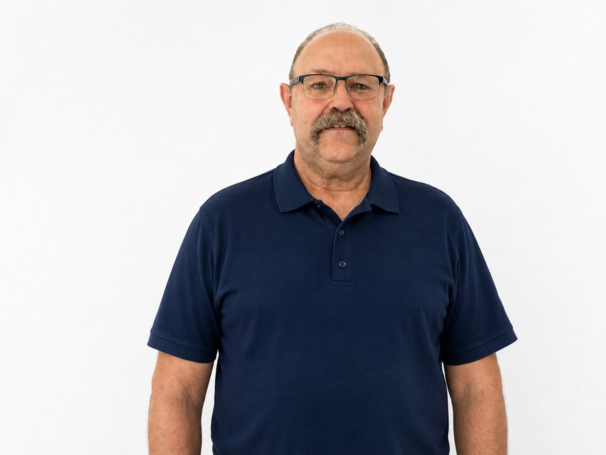Ein Mann in einem grünen Pullover lächelt vor einer weißen Wand in die Kamera.