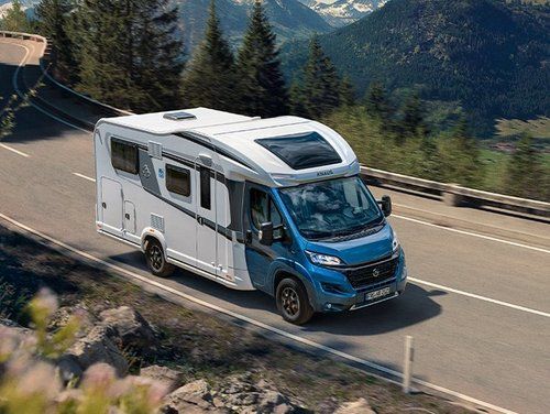 Wohnmobil fährt auf einer Bergstraße; blau-weiße Außenlackierung; Naturkulisse.