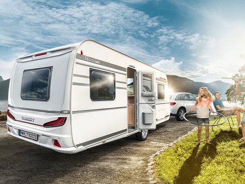 Ein weißer Wohnwagen steht in der Nähe eines Sees, eine Familie genießt die Natur.