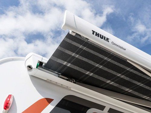 Weiße Thule-Markise an einem Wohnmobil, teilweise ausgefahren, schwarz-grau gemusterter Stoff vor bewölktem Himmel.