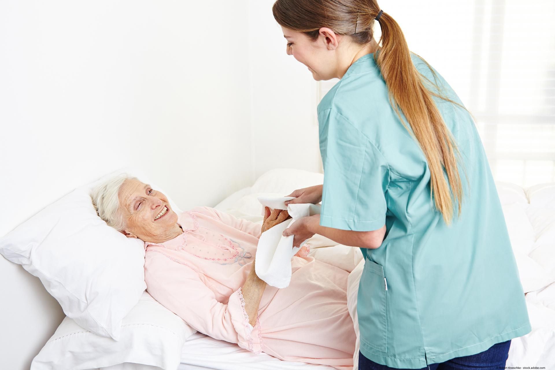 Lächelnde Krankenschwester versorgt Seniorin im Krankenbett.