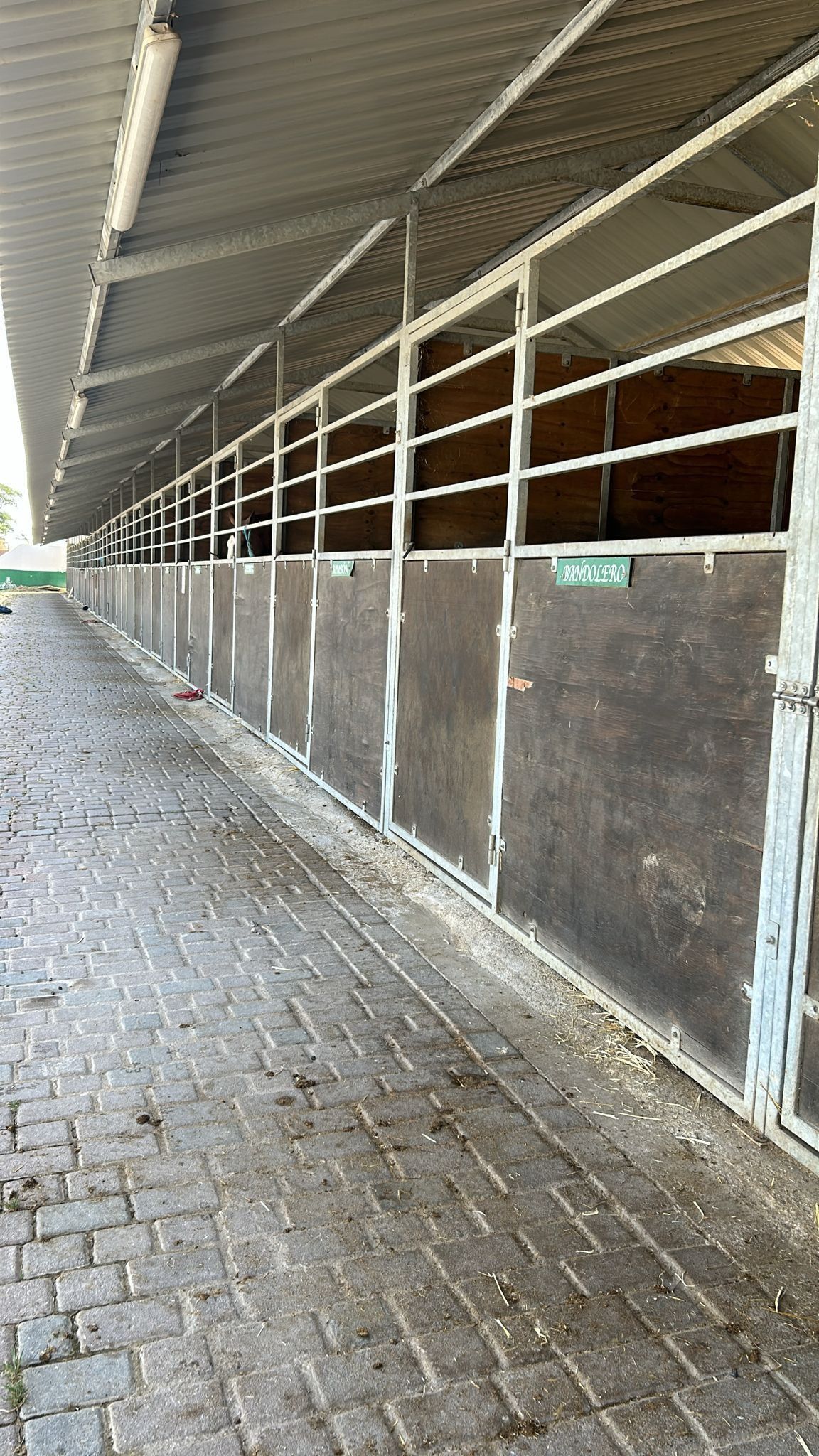 Pasarela cubierta junto a los establos con puertas metálicas y suelo pavimentado.