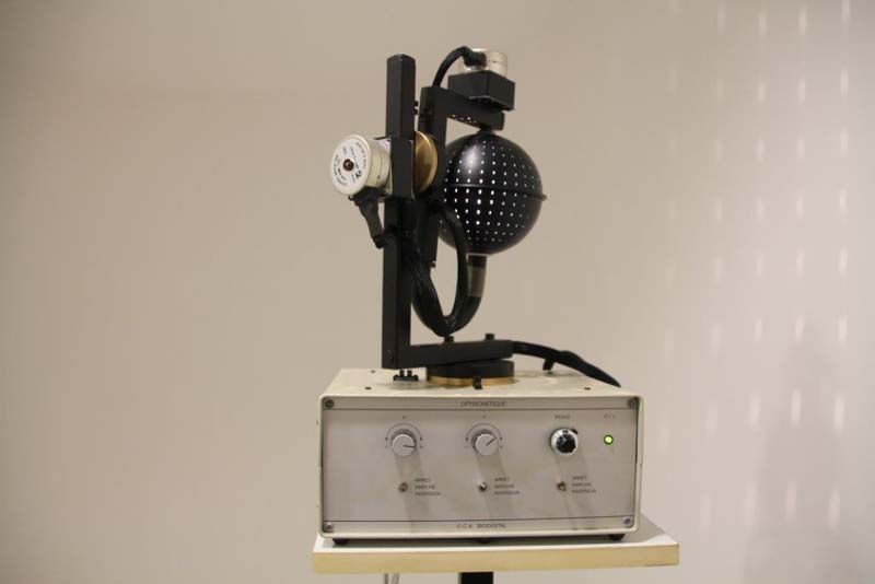 Máquina quirúrgica antigua con brazo articulado negro y lámpara en forma de cúpula sobre una caja de control beige.