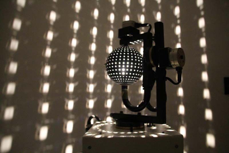 Un foco de escenario con un patrón en blanco y negro proyecta sombras punteadas sobre una pared.