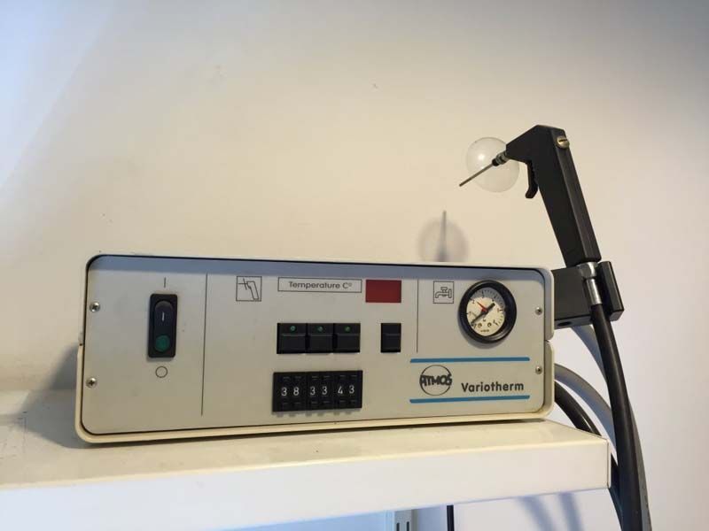 Dispositivo de laboratorio con panel de control, manómetro y brazo negro sobre un estante blanco.