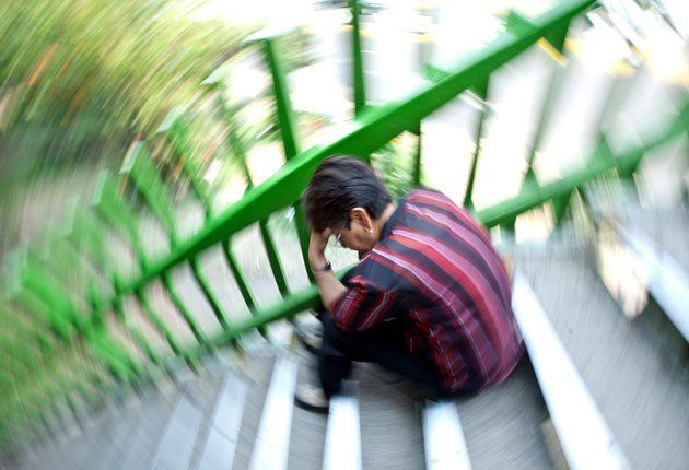 Persona sentada en unas escaleras junto a una barandilla verde, con la cabeza entre las manos y con un desenfoque de movimiento a su alrededor.