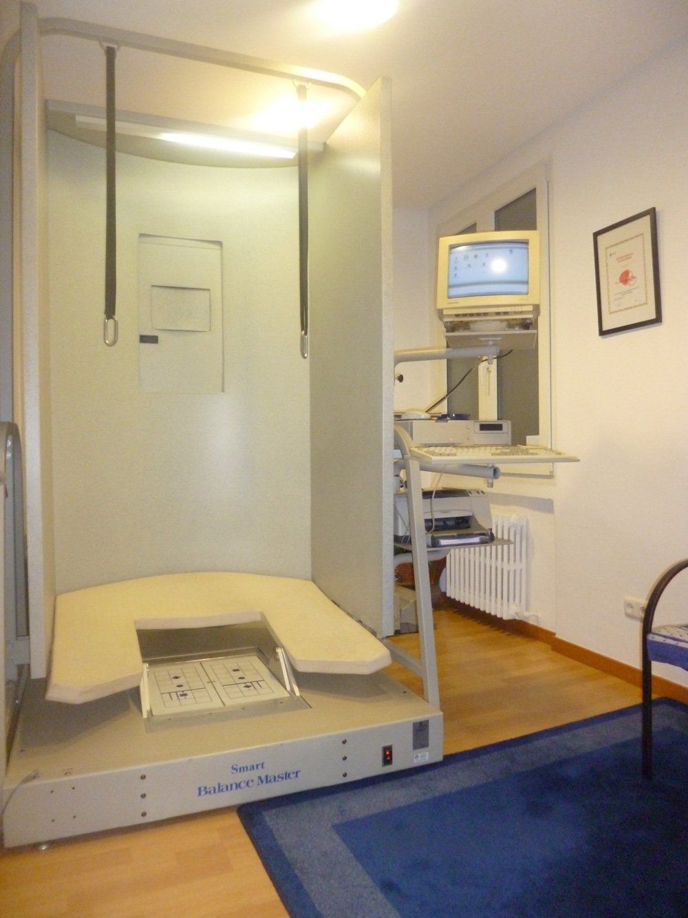 Escáner de imágenes médicas compacto en una habitación pequeña con alfombra azul y un monitor de computadora cerca.