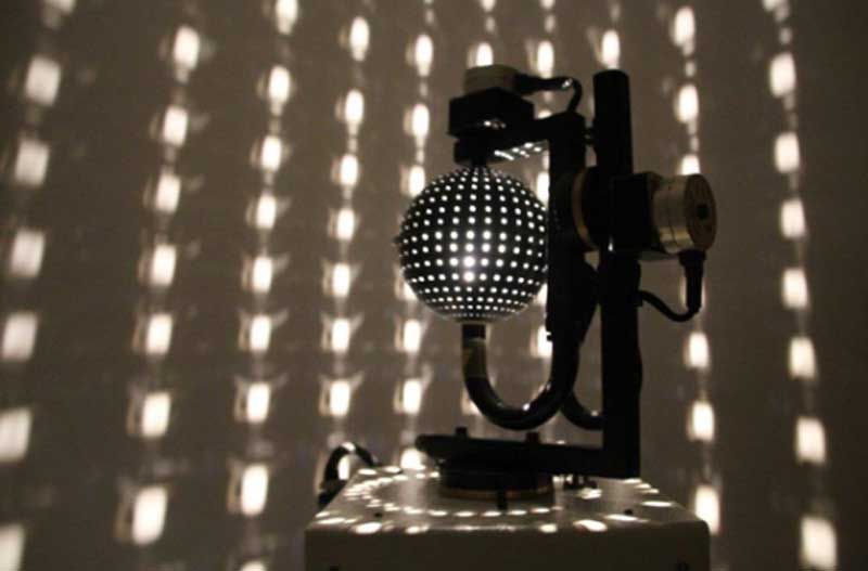 Una lámpara con forma de bola de discoteca que proyecta patrones de luz punteada sobre una pared en una habitación oscura.