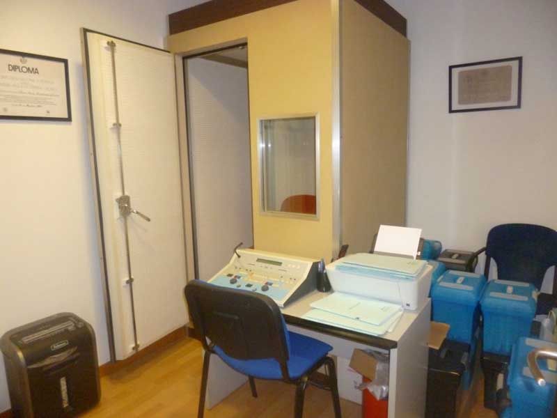 Pequeña oficina con escritorio, silla azul, impresora, archivador y puerta abierta a otra habitación.
