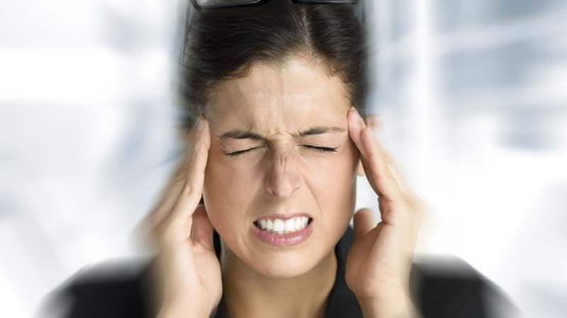 Mujer con los ojos cerrados, haciendo una mueca y sujetándose las sienes como si sintiera dolor o dolor de cabeza.