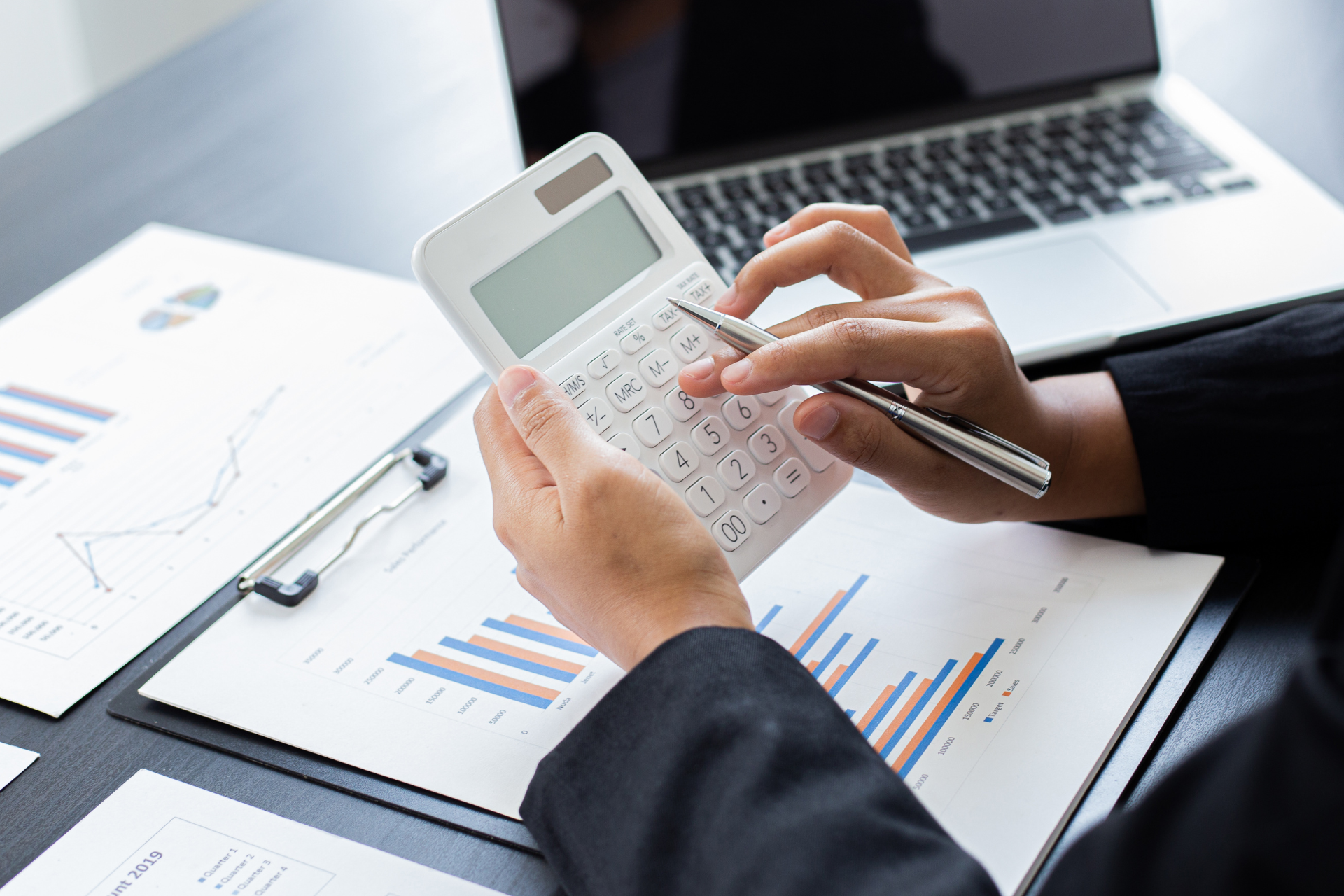 Una mujer está usando una calculadora y un bolígrafo mientras está sentada en un escritorio.