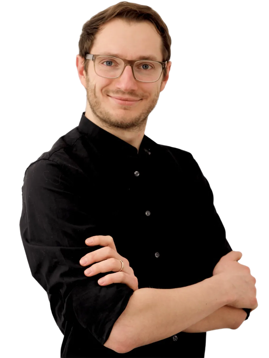 Person in schwarzem Hemd und Brille, die mit verschränkten Armen vor einem weißen Hintergrund steht