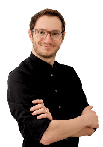 Mann mit Brille und schwarzem Hemd, lächelnd mit verschränkten Armen vor weißem Hintergrund