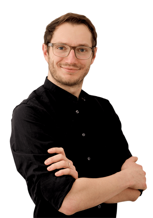 Lächelnder Mann mit Brille und schwarzem Hemd, der mit verschränkten Armen vor einem weißen Hintergrund steht