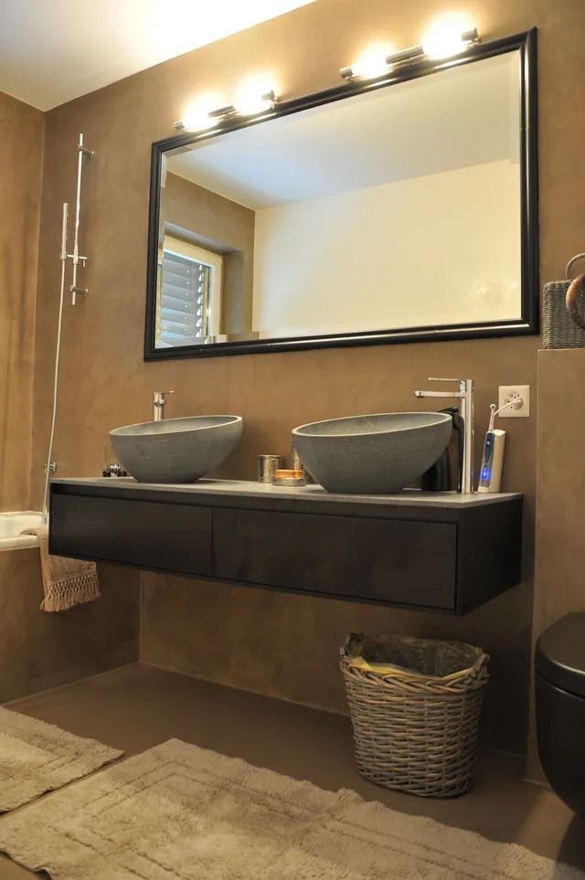 Bagno moderno con mobile lavabo sospeso scuro, due lavandini grigi, grande specchio e pareti marroni.